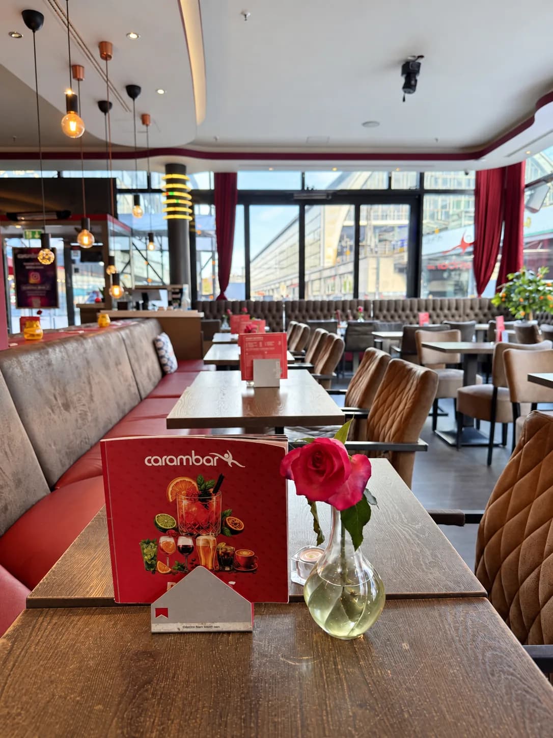 Tisch mit Rose und Karte im Restaurant der Carambar, dahinter Sitzbänke und Fensterfront